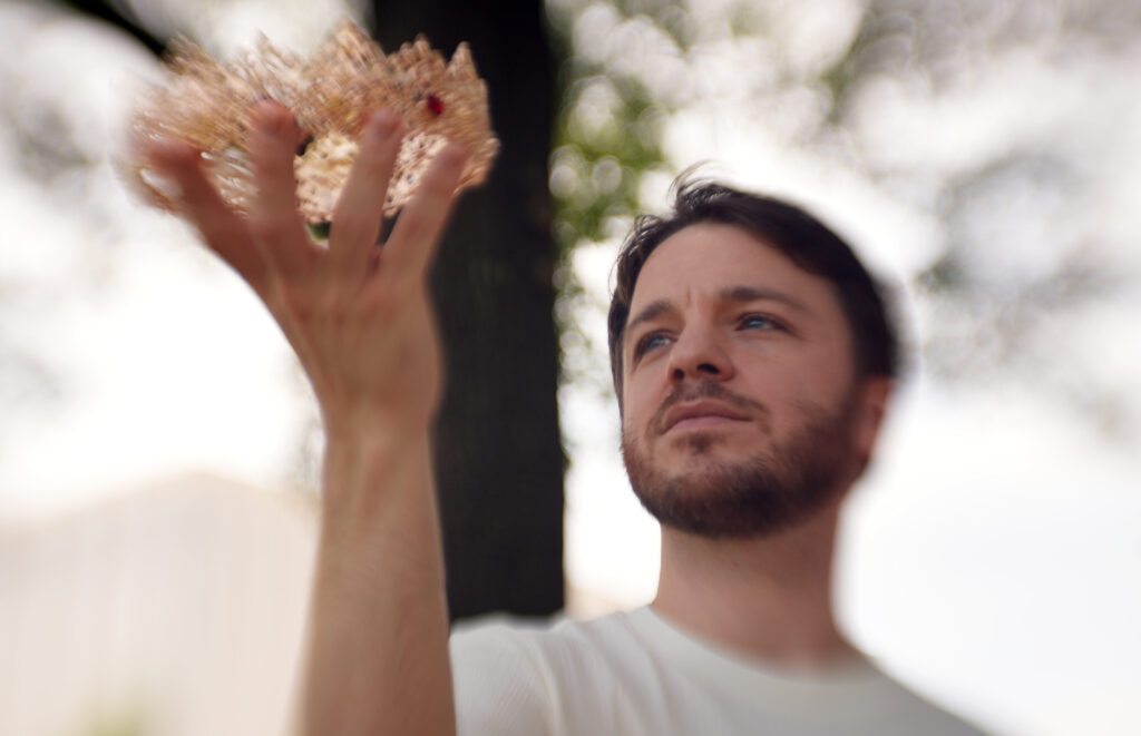 Man holds a crown in the foreground with a tree in the background